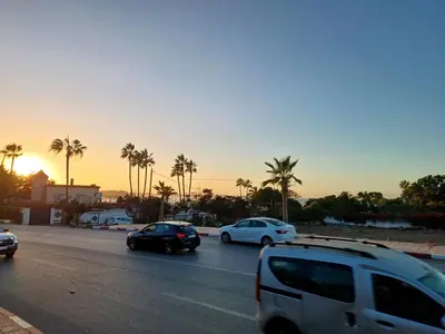 a group of cars driving down a street with palm trees at الشروق 2 in Mansouria