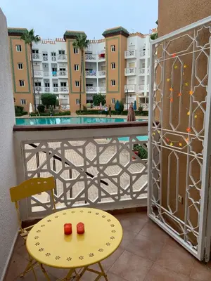 a table and a chair on a balcony with a pool at Al kawtar Vacation apartment in Mansouria in O Ben Slimane