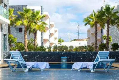 a swimming pool with two blue chairs and palm trees at Garden Bay Luxe, Tamaris Bord de Mer in Casablanca