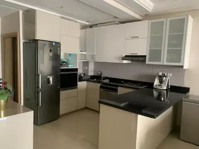 a kitchen with white cabinets and a stainless steel refrigerator at Appartement avec Terrasse, Piscine & Plage à Ola Blanca 2 in Sidi Rahal