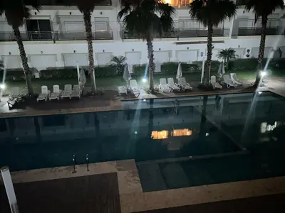 a swimming pool with chairs and palm trees in a hotel at Kettani Shems Bouznika in Bouznika