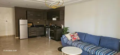 a living room with a blue couch and a kitchen at Appartement tamaris in Sidi Rahal