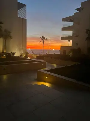 a sunset at the beach with a building and palm trees at beach front gardens in Mohammedia