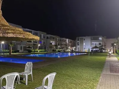 two white chairs sitting in the grass by a pool at night at Sunset Malaga beach house in Mansouria