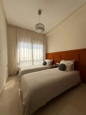 two beds in a hotel room with a window at Appartement moderne avec piscine, 2 chambres in Bouznika