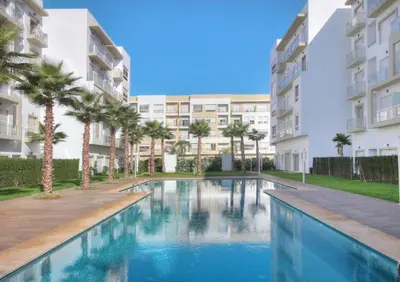 a swimming pool with palm trees and buildings at Appartement bouznika in Bouznika