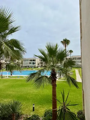 a palm tree in a park with a swimming pool at OlaBlanca2, appartement avec terrasse et vue sur piscine in Sidi Rahal