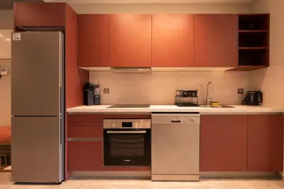 a kitchen with brown cabinets and a stainless steel refrigerator at Studio 1BR Near CFC - 5 Stars Experience in LʼOasis