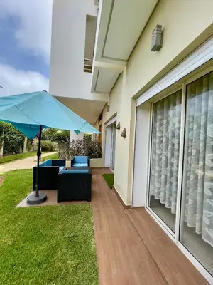 a patio with a blue umbrella next to a house at Appartement Pied dans l'eau avec terrasse-Casa bay in Sidi Rahal