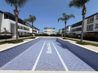 a swimming pool with palm trees in front of apartments at Eden Prestige in Bouznika
