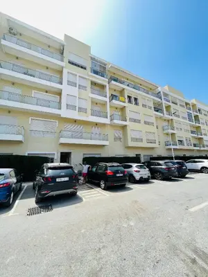 a large apartment building with cars parked in a parking lot at Bel appartement vue piscine in Bouznika
