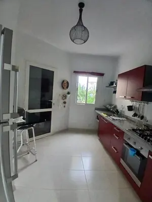 a kitchen with red cabinets and a sink and a window at Appartement BAHIA BEACH piscine plage privée in Bouznika