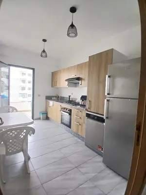 a kitchen with a stainless steel refrigerator and a table at Duplex Luxe 3 Chambres Vue Mer & Piscine à Zenata Eco City in Aïn Harrouda
