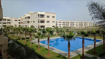 a pool with palm trees in front of a building at 2 Bedroom Apartment in Mohammedia