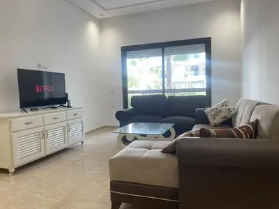 a living room with a couch and a tv at Appartement Luxe Vue Piscine Résidence Les Perles de Bentriaa, El Mansouria in Mohammedia