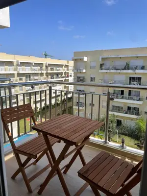 a wooden table and chair on a balcony with a building at lumineux appartement in Bouznika