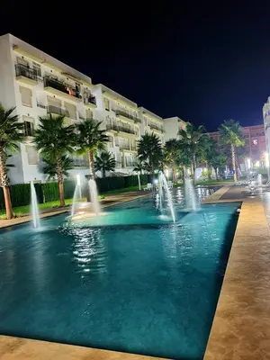 a swimming pool with fountains in front of a building at Appartement vue sur piscine kettani in Bouznika