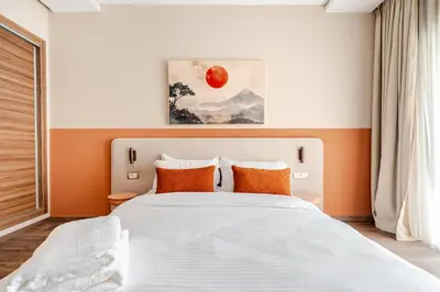 a bedroom with a large white bed with orange pillows at 5 min from airport, 1 bedroom, balcony, pools in Nouaceur