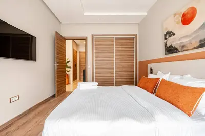 a bedroom with a large white bed with orange pillows at 5 min from airport, 1 bedroom, balcony, pools in Nouaceur