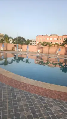 a pool of water with chairs and buildings in the background at Kasbah de bouznika, style Marrakech avec jardin et piscine in Kasba Bou Hamira