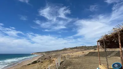 a view of a beach with the ocean and a straw hut at Bel appartement centre Asilah proche de la mer in Aïn Harrouda