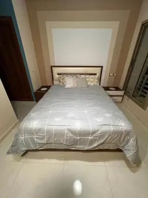 a bed with a white comforter in a bedroom at Appartement Chaleureux in Bouznika