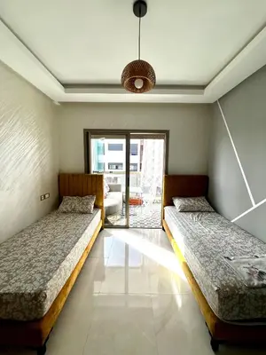 two beds in a room with a window at Appartement Chaleureux in Bouznika