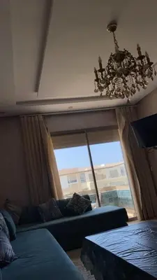 a living room with a blue couch and a chandelier at Appartement dans une résidence fermée, Malaga Beach in Mohammedia