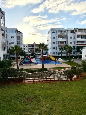 a playground with a slide in a park with buildings at Charmant Appart 5 minutes de La Plage Sablette in Mohammedia