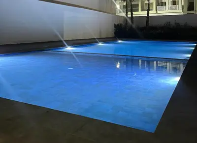 a blue swimming pool with lights in a building at Appartement calme in Bouznika