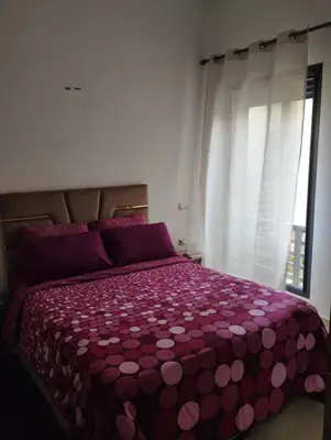 a bedroom with a bed with a purple comforter and a window at Appartement à louer à Bouznika avec piscine in Bouznika