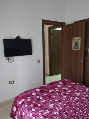 a bedroom with a purple bedspread with a television on the wall at Appartement à louer à Bouznika avec piscine in Bouznika