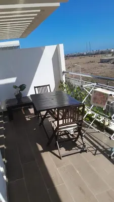 a picnic table and chairs on a balcony with a beach at residence ramo flores in Bir Jedíd Saint-Hubert