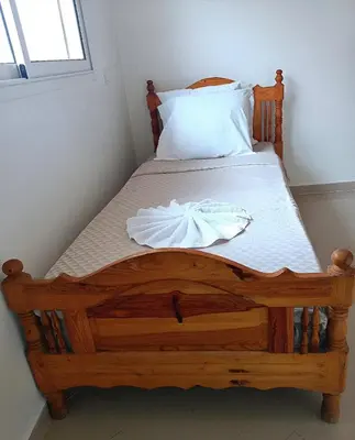 a bedroom with a wooden bed with a white sheets at Kridarek - Bel appartement avec piscine in Sidi Rahal