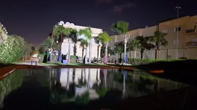 a building with palm trees and a reflecting pool at night at Appart Coquette à Tamariss in Tamaris