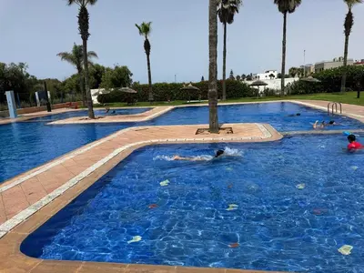 a group of people swimming in a pool with palm trees at Modern appartment in Casablanca