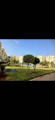 a park with a tree and buildings in the background at Séjour Idéal Piscine & Sécurité in Bouznika