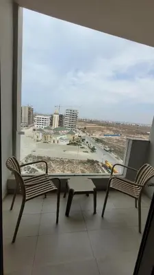 a balcony with two chairs and a table and a large window at Appartement Neuf & Cosy avec vu sur mer -Zenata Eco City- in Aïn Harrouda
