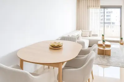 a white living room with a wooden table and chairs at Kridarek - Appartement chic et cosy à Casa Finance City in Casablanca
