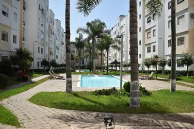 a swimming pool with palm trees and buildings at Kridarek - Bel appartement avec piscine à Dar Bouazza in Tamaris