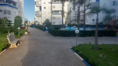 a park with a bench and palm trees and buildings at La vie de vacances fal azur in Bouznika
