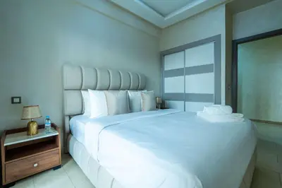 a bedroom with a large white bed and a night stand at Appartement Élégant au Cœur de Central Park in Mohammedia