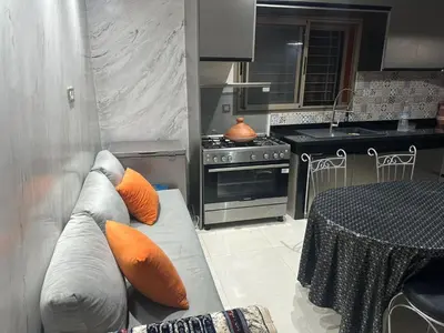 a kitchen with a couch with orange pillows and a table at Belle maison avec piscine à 7 min de la plage en voiture in Dar Bouazza