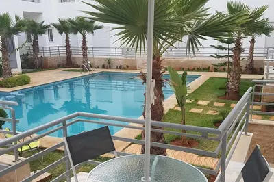 a swimming pool with a table and palm trees at Sables d'or flat apartement in El Harhoura