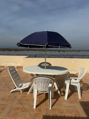 a table and chairs with an umbrella on the beach at Joumaira beach in Temara