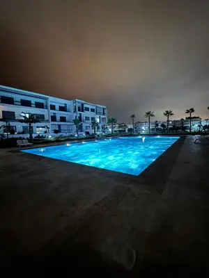 a large swimming pool in front of a building at night at Jolie appartement piscine bord de mer Haut standing in Mansouria