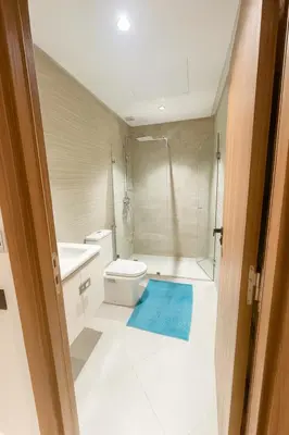 a bathroom with a toilet and a shower with a blue rug at Jolie appartement piscine bord de mer Haut standing in Mansouria