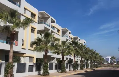 a building with palm trees in front of it at Appartement de haut standing à EL MANSOURIA residence EBLA in Pont Blondin