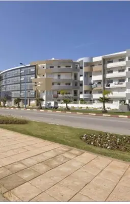 a city street with a large apartment building in the background at Magnifique Appartement à Louer C14 Jnane Dalya in Bouznika