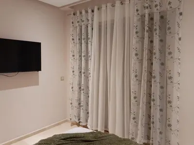a bedroom with white curtains and a flat screen tv at Les belles loges in Bouskoura